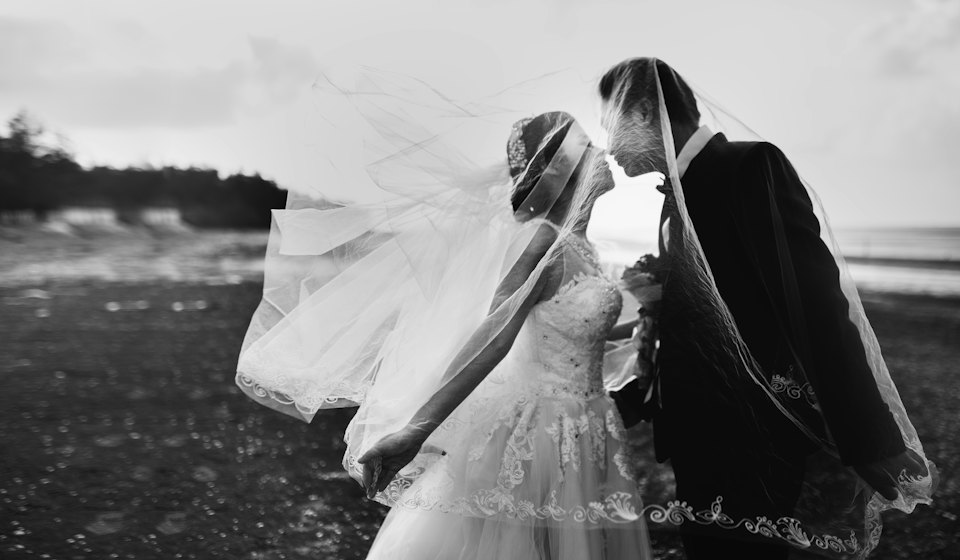 Black-and-white photograph of a couple about to kiss as the wind lifts the veil.